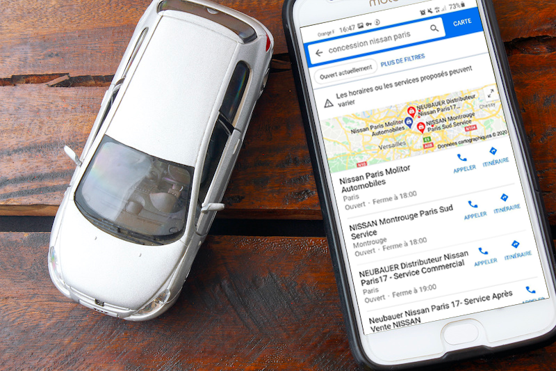 Une petite voiture sur une table à côté d'un smartphone sur une page de recherche google sur concessionnaire paris